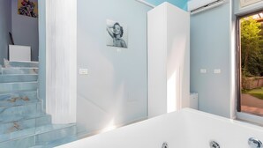 Un baño moderno con bañera, una escalera y una ventana con vistas a la vegetación.