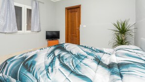 Un dormitorio con una cama, un televisor sobre un soporte de madera, una puerta y una planta en maceta.