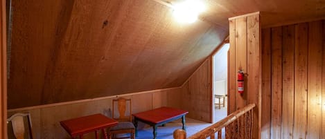 A wooden attic room with two red tables, a chair, and a wooden railing.