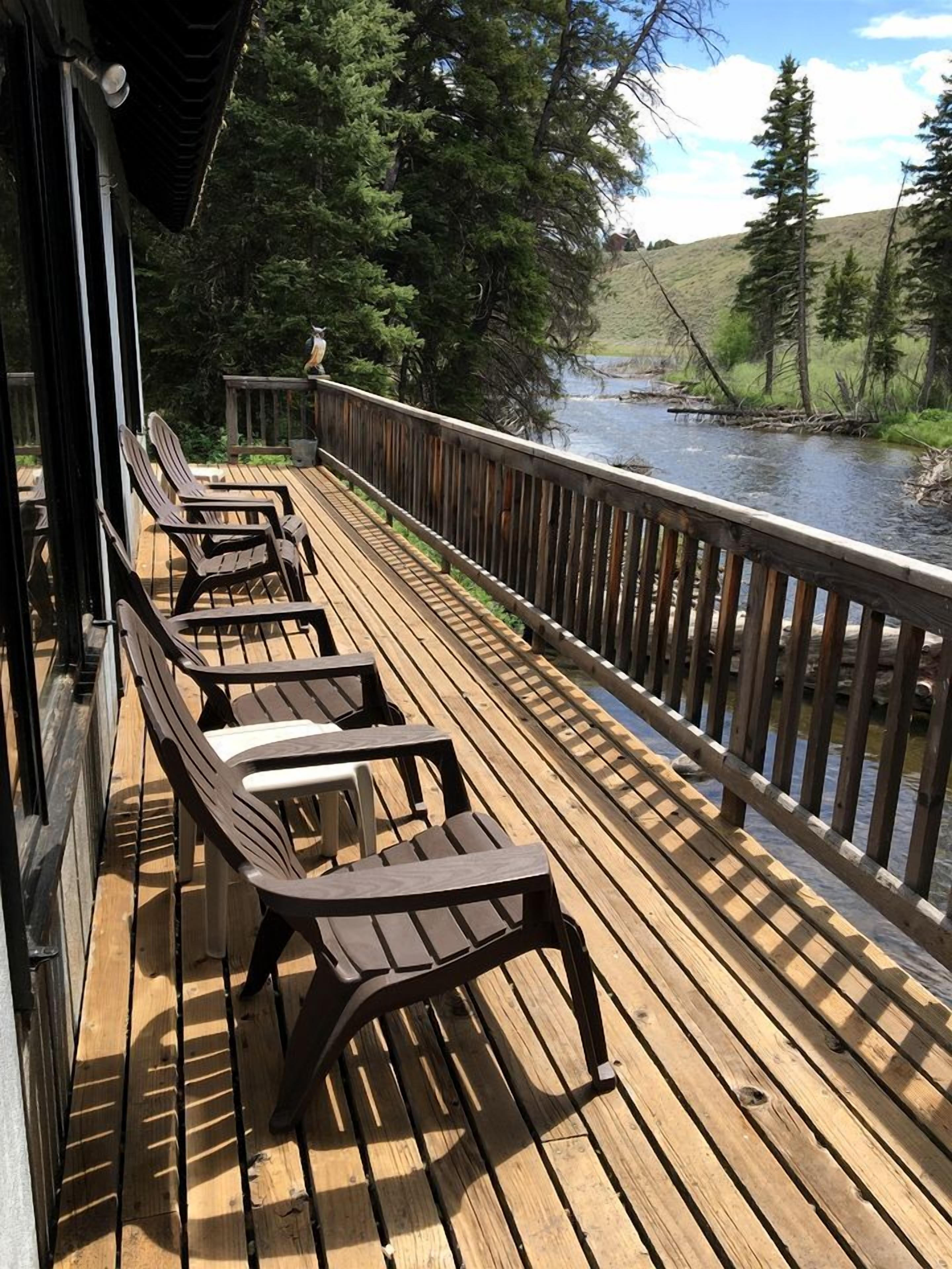 Terraza de madera con sillas que da a un río, rodeada de árboles.