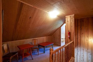 A wooden attic room with two red tables, a chair, and a wooden railing.