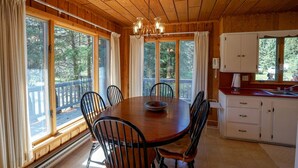 Une cabane en bois comprenant une table et des chaises, un lustre et un coin cuisine avec des placards et une fenêtre.