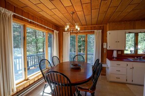 A wooden cabin with a dining table and chairs, a chandelier, and a kitchen area with cabinets and a window.