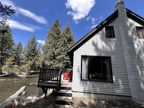 A cabin with a deck overlooking a river, surrounded by trees.
