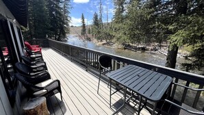 Eine Holzterrasse mit Außenmöbeln, mit Blick auf einen Fluss und ein bewaldetes Gebiet.