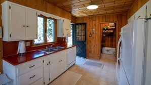 Une cuisine de taille réduite avec des murs en bois et un sol carrelé, comprenant un évier, des placards et un réfrigérateur.