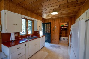 A compact kitchen with wooden walls and a tiled floor, featuring a sink, cabinets, and a refrigerator.