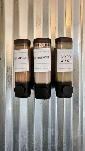 Three bottles of shampoo, conditioner, and body wash on a metal surface.