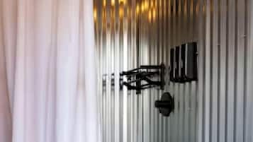 A bathroom with a white toilet, a shower with a black hose, and a metal wall.