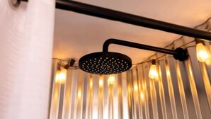 A shower with a black handle and a circular head, mounted on a wall with a curtain.