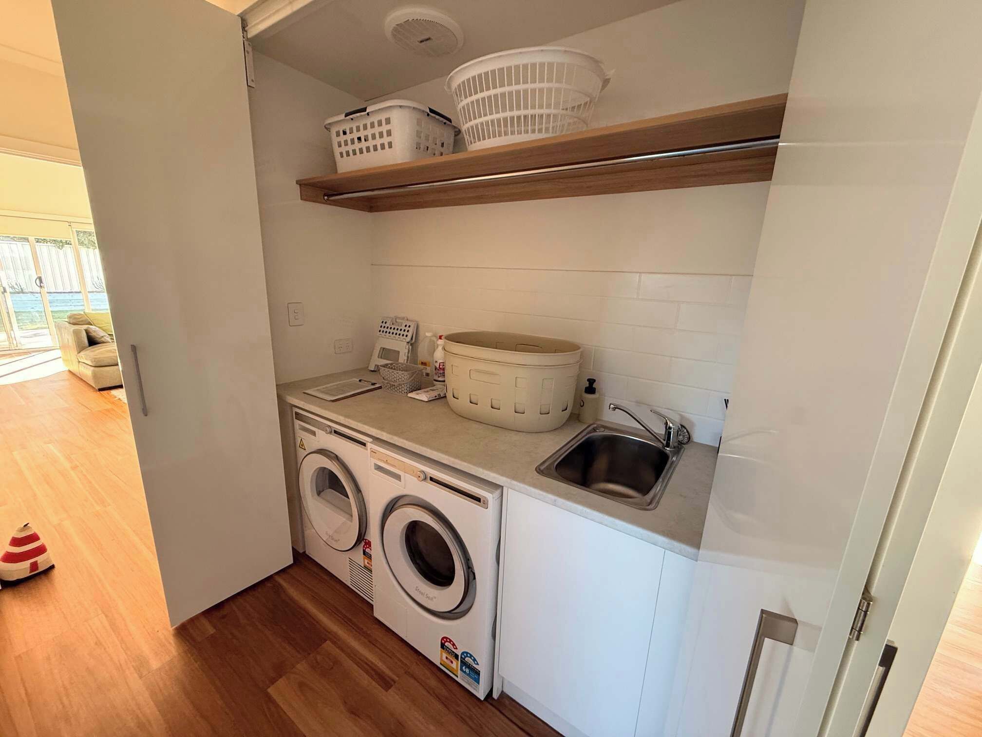 A compact laundry area with a washing machine, a sink, and storage shelves.