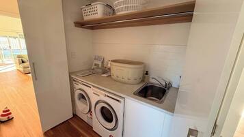 A compact laundry area with a washing machine, a sink, and storage shelves.