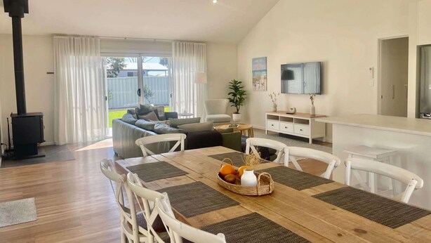 A modern living room with a dining area, a fireplace, a TV, and a view of the outdoors. - The Salty Olive - WiFi, Pet Friendly Outside (Robe)