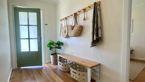 A hallway with a wooden bench, baskets, a potted plant, and a coat rack with bags. - The Salty Olive - WiFi, Pet Friendly Outside (Robe)