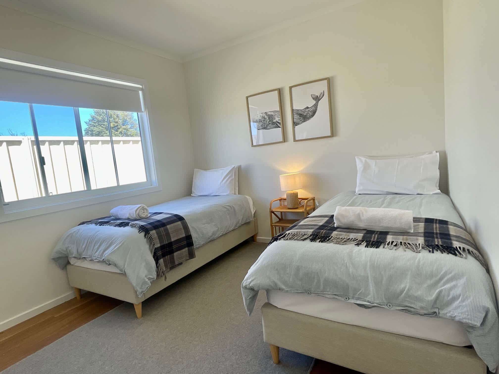 A bedroom with two beds, a window, a nightstand, and two framed pictures on the wall.