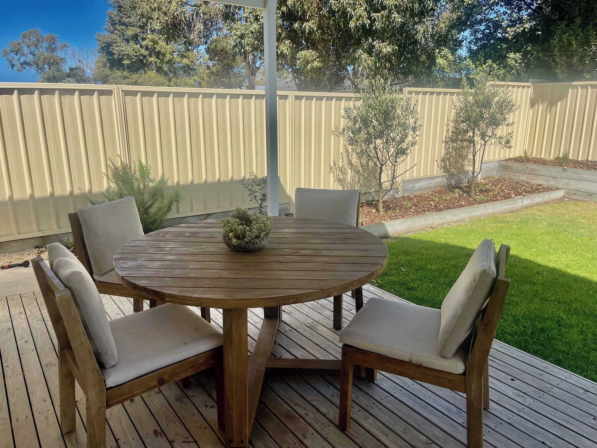 A wooden deck with a round table and four chairs, surrounded by a wooden fence and a grassy yard.