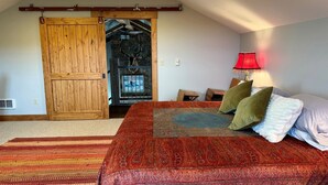 Quarto com uma cama grande, porta de madeira, abajur vermelho e vista para o exterior.