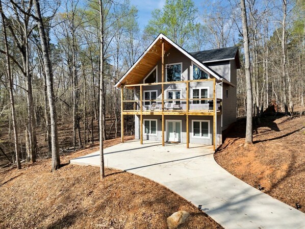 Une maison à deux étages avec un balcon, entourée d’une zone boisée.