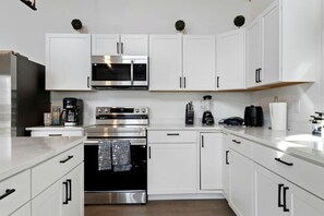 A modern kitchen with white cabinetry, stainless steel appliances, and a wooden countertop.