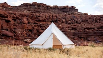 A white tent in a grassy field with a rocky backdrop.