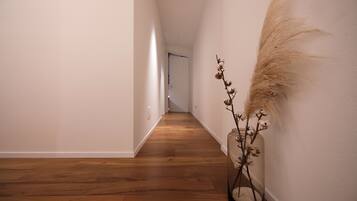 Un pasillo con suelo de madera y un jarrón con plantas secas en la pared derecha.