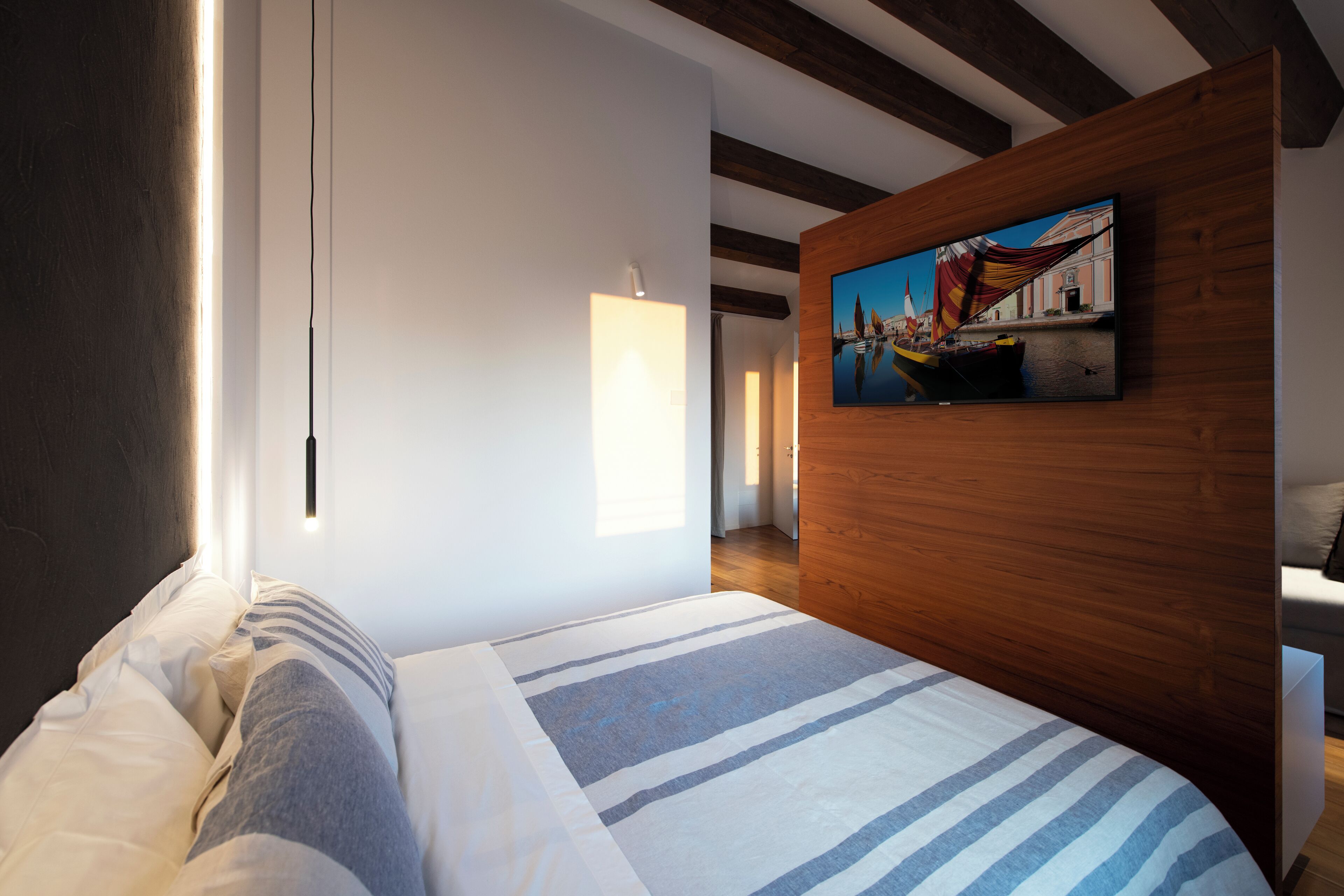 Una habitación de hotel moderna con una cama grande, un panel de madera decorativo y un televisor montado en la pared.