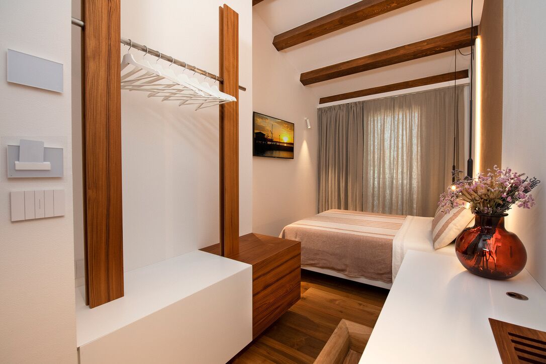 Un dormitorio moderno con un armario de madera, una mesita de noche con un jarrón y una cama con una colcha a rayas.