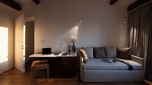 Ein modernes Wohnzimmer mit einer Couch, einem Schreibtisch mit Laptop, einem Sessel und einem Fenster mit Vorhängen.