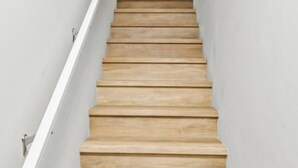 Eine schmale Holztreppe mit weißen Wänden und einem Geländer auf einer Seite.