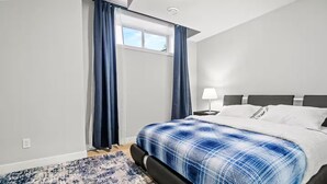 Ein modernes Hotelzimmer mit einem großen Bett, einem Nachttisch mit Lampe und Blick ins Freie durch ein Fenster mit Vorhängen.