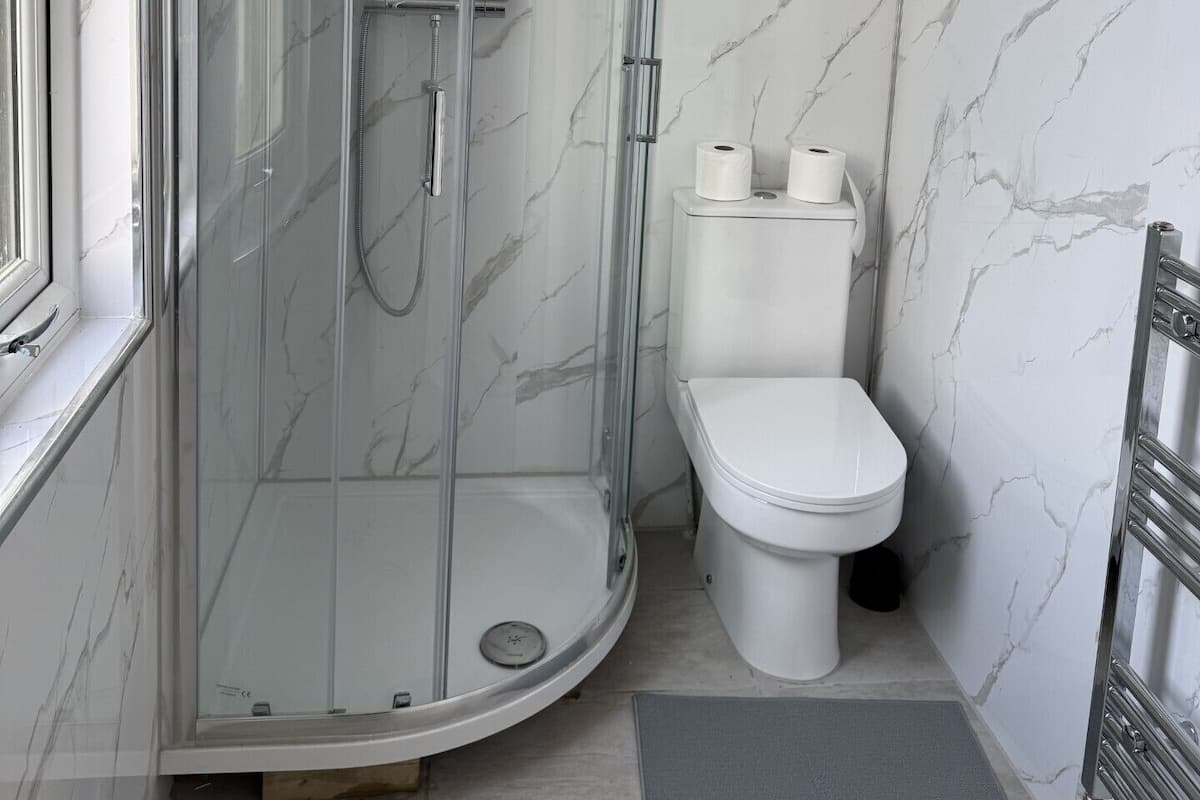A modern bathroom with a glass-enclosed shower, a toilet, and marble walls.