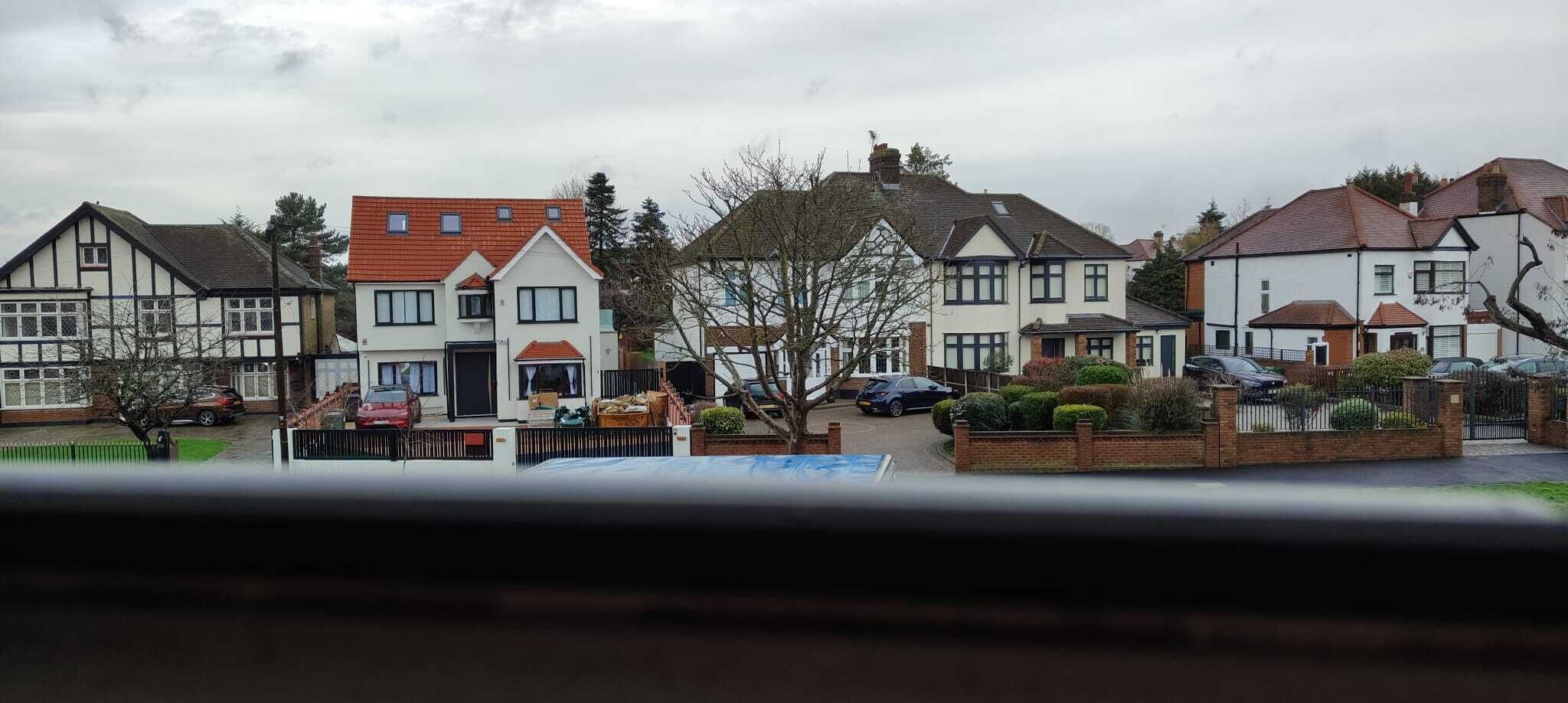 Een rij herenhuizen met puntige daken, een oprit en een geparkeerde auto.