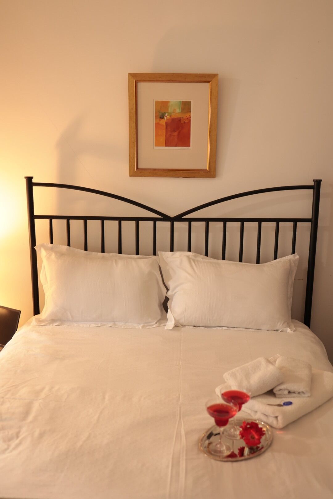 Un letto con struttura in metallo, biancheria bianca e un quadro appeso sopra.