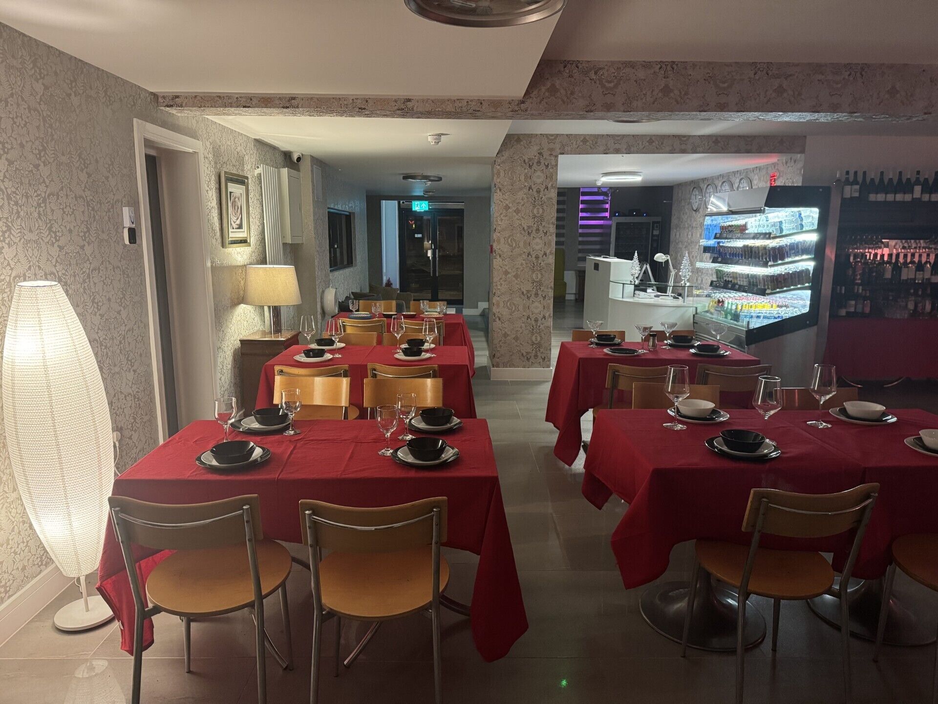Un restaurante con manteles rojos, sillas de madera y una zona de bar con botellas de vino.