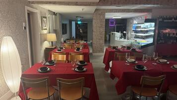 Un restaurante con manteles rojos, sillas de madera y una zona de bar con botellas de vino.