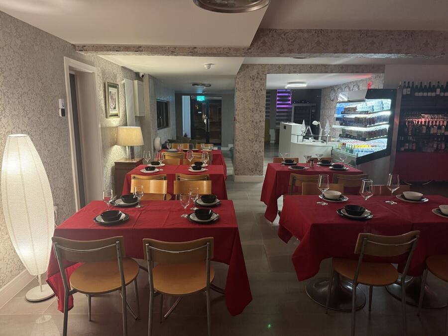 Un restaurante con manteles rojos, sillas de madera y una zona de bar con botellas de vino.