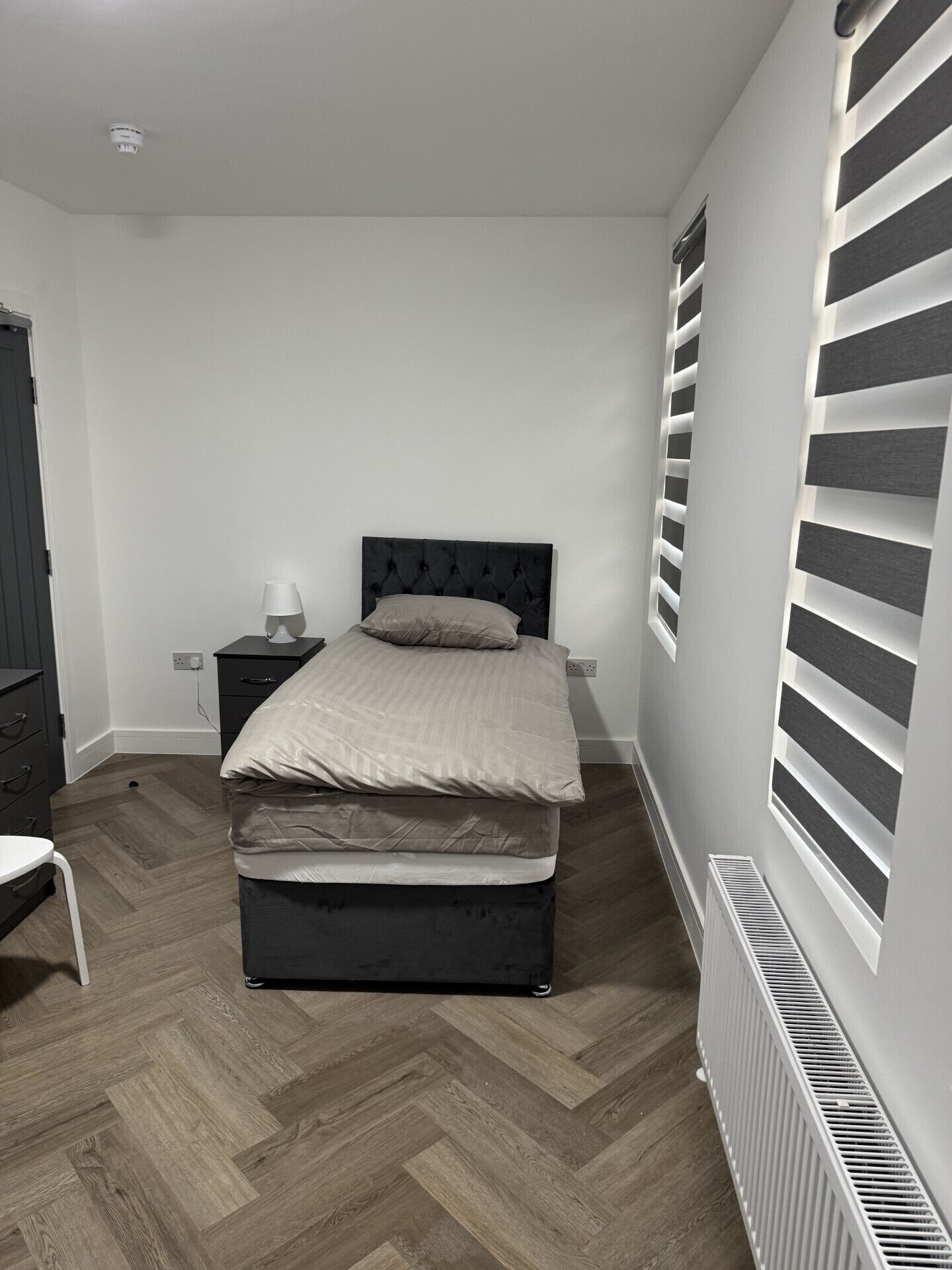 A bedroom with a bed, bedside table, lamp, and a radiator.