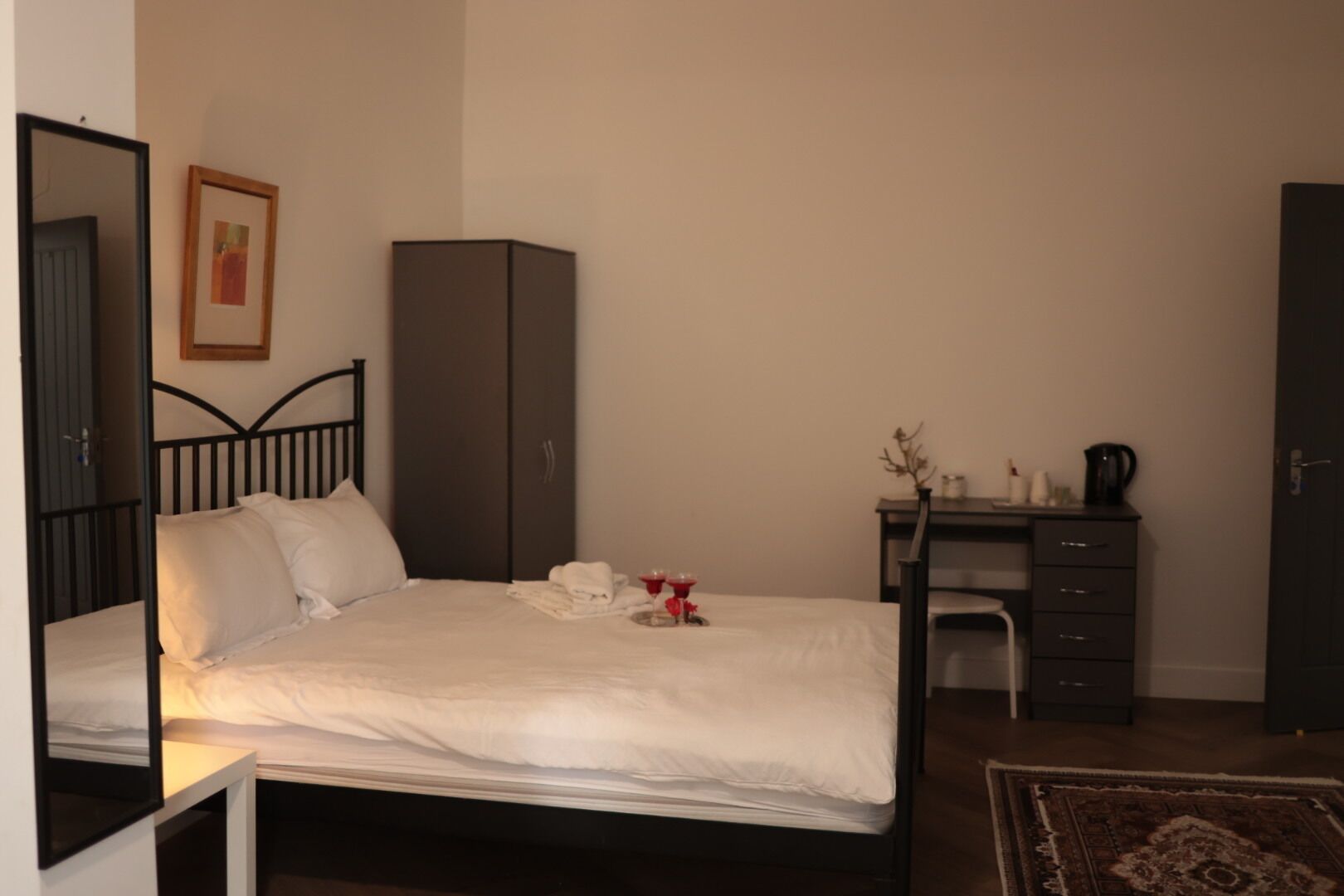 A bedroom with a bed, a wardrobe, a desk, and a mirror.