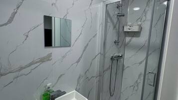 A modern bathroom with a marble wall, a glass shower enclosure, and a vanity with a mirror and toiletries.