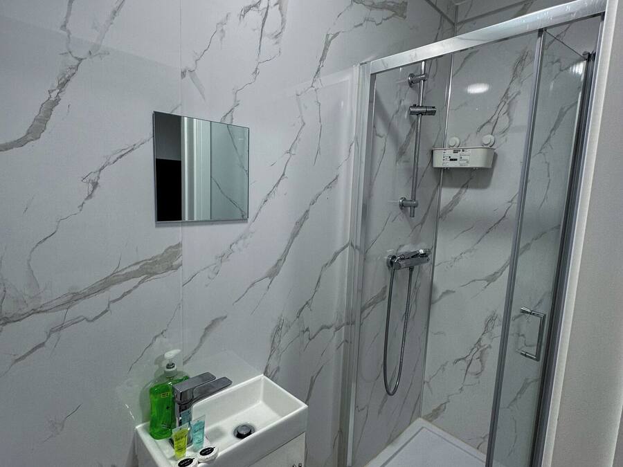 A modern bathroom with a marble wall, a glass shower enclosure, and a vanity with a mirror and toiletries.