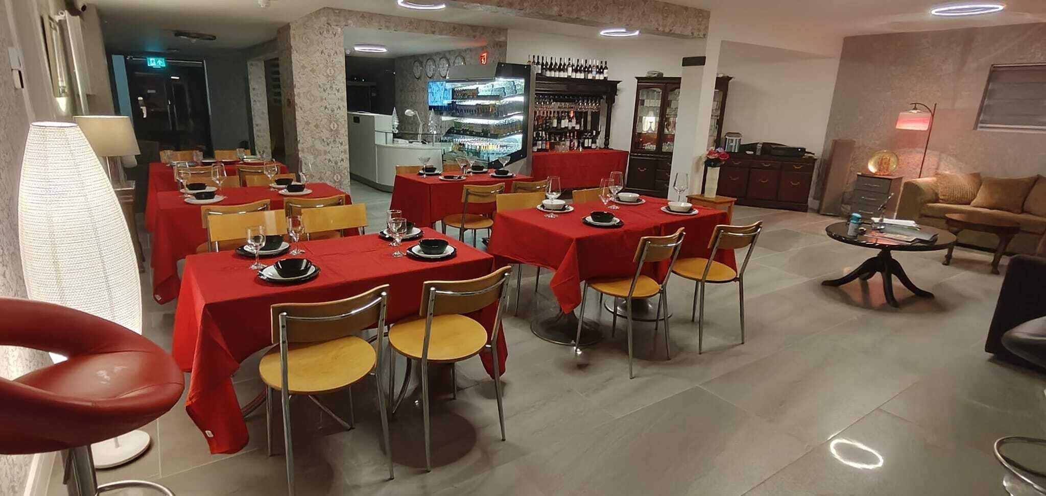 Un ristorante con diversi tavoli apparecchiati per consumare i pasti, una zona bar con bottiglie di vino e un'area salotto con divano e lampada.