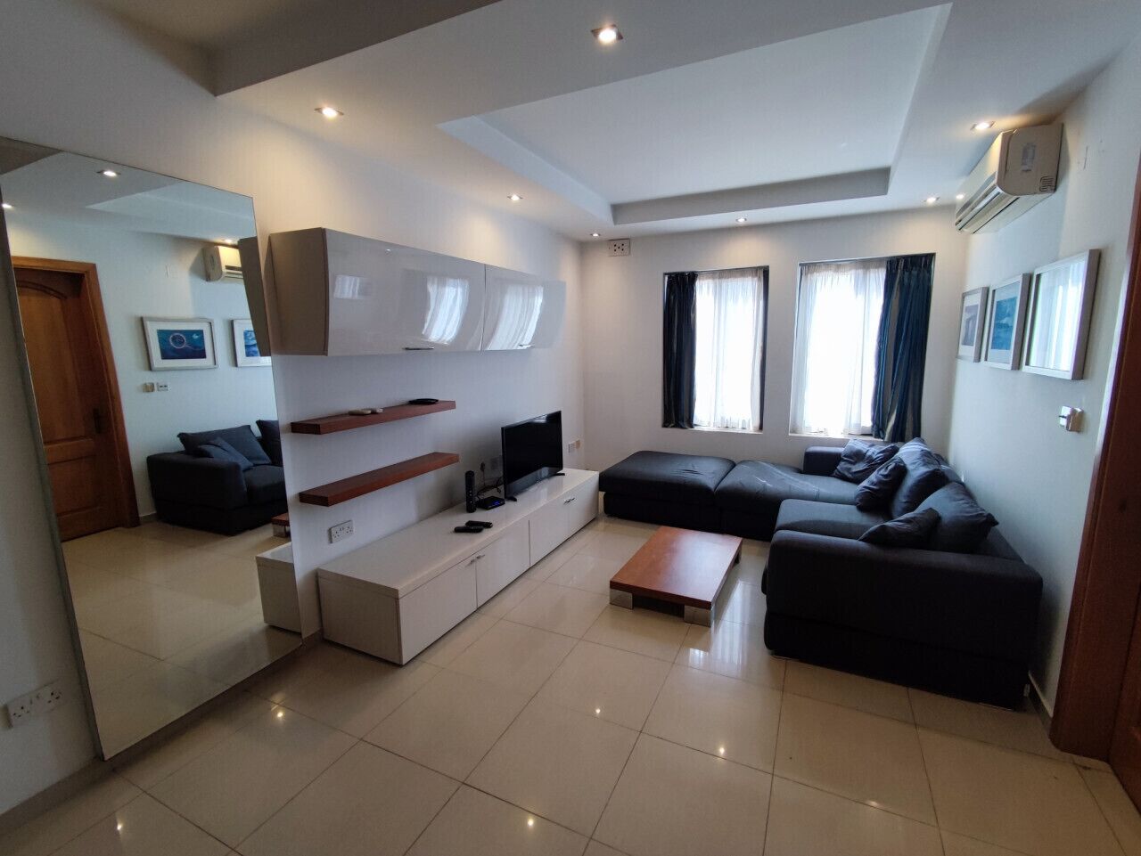 A modern living room with a flat-screen TV, a sofa, a coffee table, and a large mirror.