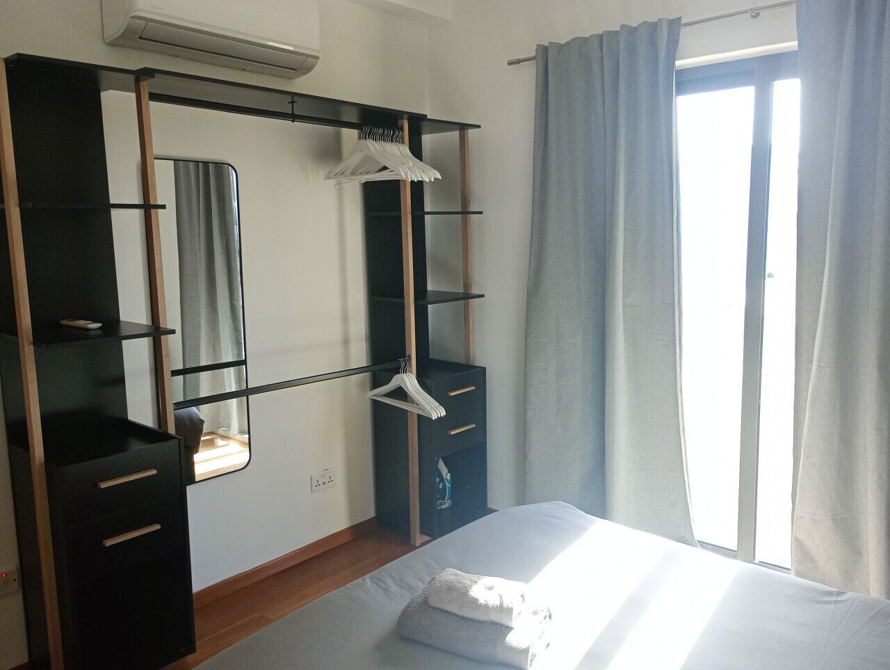 Ein Schlafzimmer mit Bett, Kleiderschrank, Spiegel und einem Fenster mit Vorhängen.
