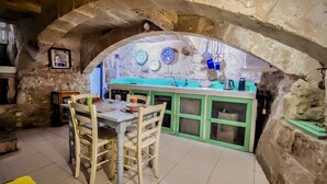 Una cucina rustica con un arco in pietra, sedie di legno, un tavolo e un armadietto verde.