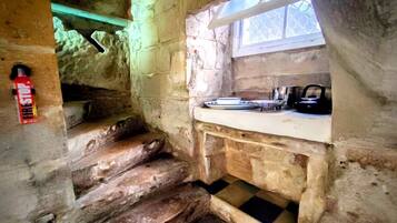 Un interior rústico de piedra con una escalera de madera, una ventana pequeña y una zona de lavamanos.