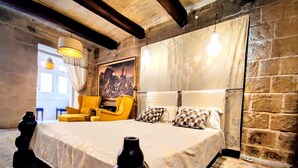 Una camera da letto con un letto grande, una poltrona gialla, un quadro appeso e un pavimento decorato.
