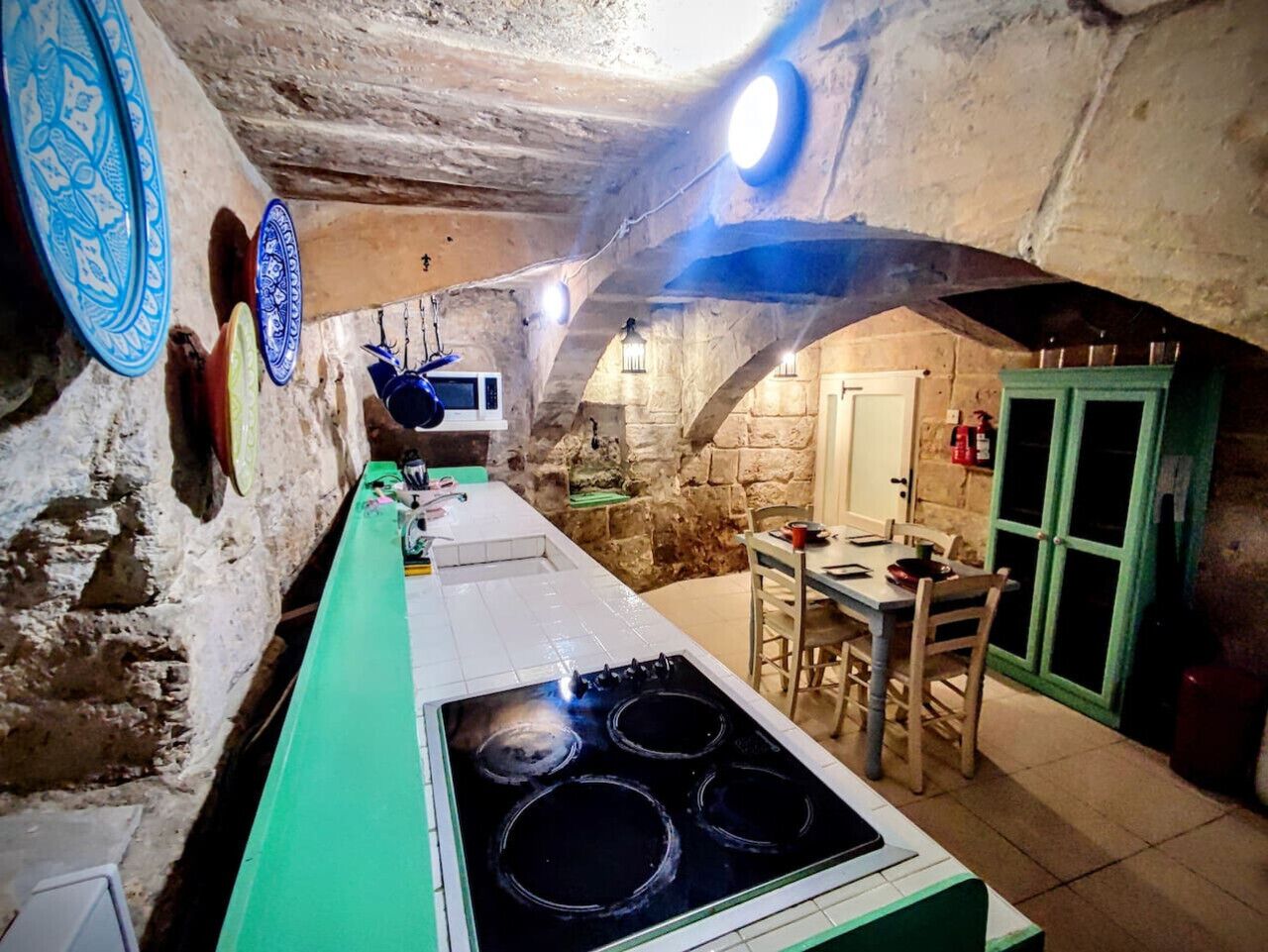 A kitchen with a stove, a dining table, and chairs. There is a stone wall and a door with a green frame.