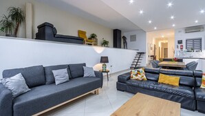 Een moderne woonkamer met een grijze bank, een houten salontafel en een zwarte leren bank met kleurrijke kussens.