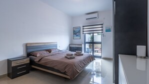 Een moderne slaapkamer met een bed, nachtkastjes, een dressoir en een raam met jaloezieën.