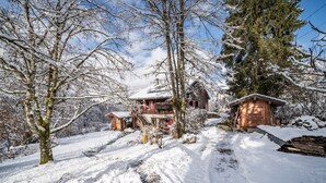 Schneebedeckte Landschaft mit Holzhütten und einem großen Baum.